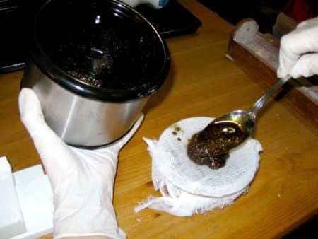 Spooning cooked cannabis-laden oil onto filter cheesecloth